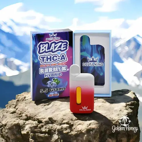 Delta King BLAZE THC-A device with Blueberry OG packaging, standing on a rocky surface against a mountain backdrop.