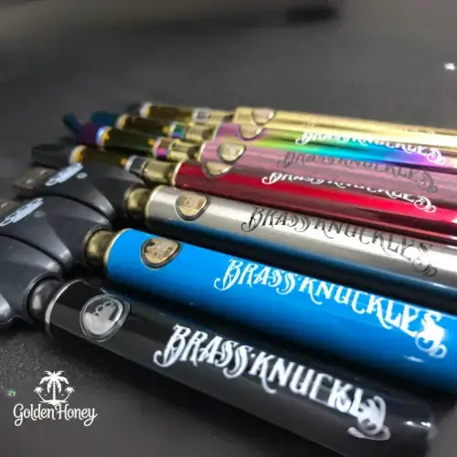 Variety of colorful THC vape pens lined up on a dark surface, showcasing the Brassy Knuckles brand.