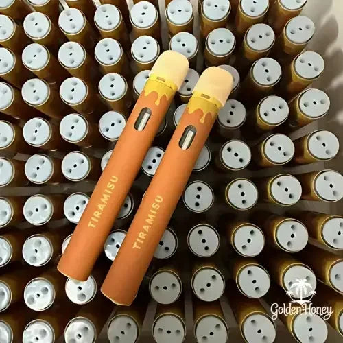 Two tiramisu-flavored vape pens surrounded by empty vape cartridges in a stylish arrangement.